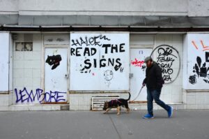 eine Person geht mit einem jungen Hund an der Leine an einer Wand entlang, das mit einem Graffitti "Read the Sings" verziert wurde. 