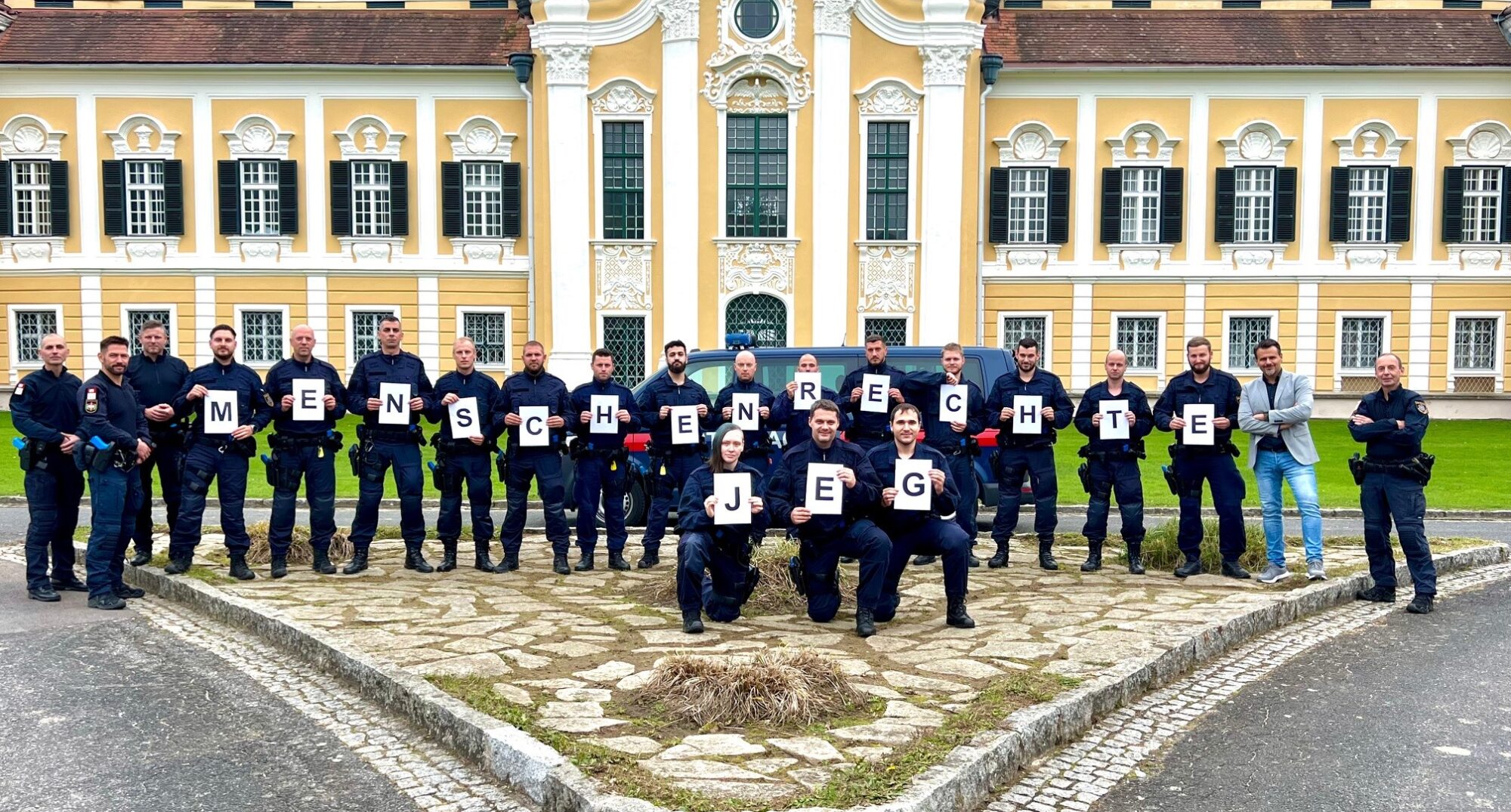 Bild 2: KontrInsp Gernot WAGNER (Bundeseinsatztrainer, Generaldirektion für den Strafvollzug und den Vollzug freiheitsentziehender Maßnahmen, Abteilung II 2 - Kompetenzstelle Sicherheit und Extremismusprävention) und Dr. Robert KRAMMER mit Mitgliedern der Einsatzgruppe der Justizwache und dem Leitspruch „Menschenrechte JEG (Justizwache Einsatzgruppe)“ (v.r.n.l.)