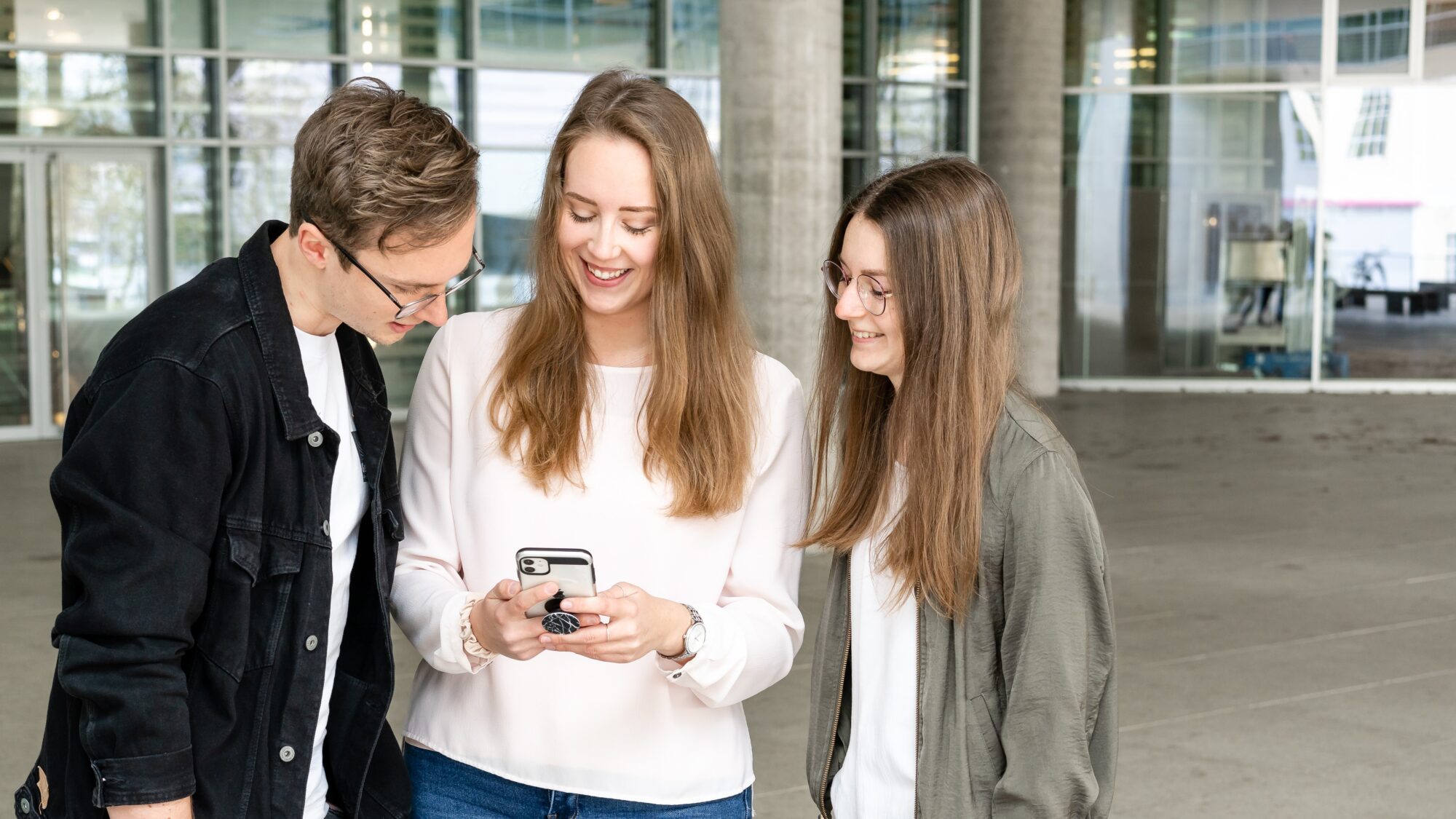 Eine Gruppe Studierender steht zusammen und blickt gemeinsam auf ein Smartphone.